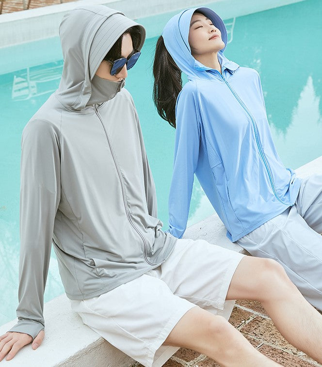 Man and woman sitting by a poolside, both wearing sun-protection jackets; the man in gray and the woman in blue.